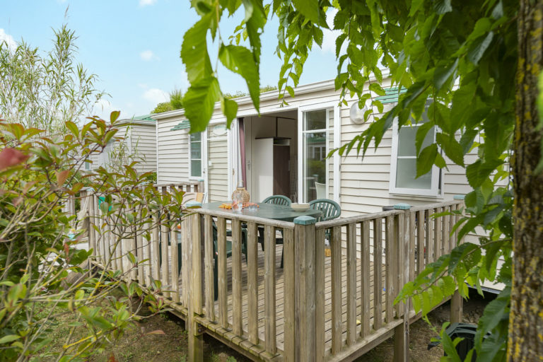 Mobil-home avec terrasse en bois dans un jardin verdoyant.