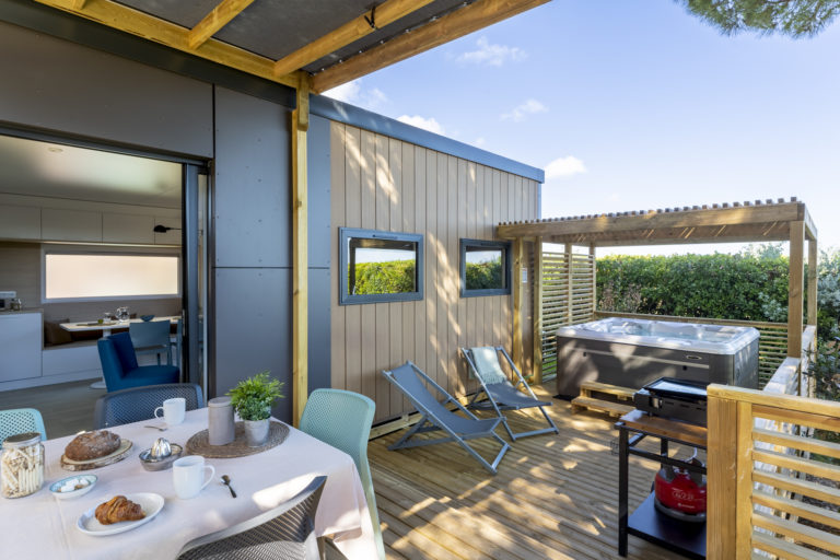 Terrasse avec jacuzzi, transats et table dressée.